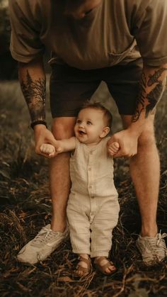 a man holding the hand of a baby in front of his face while standing on grass