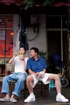 a man and woman sitting on a bench drinking tea together in front of a store