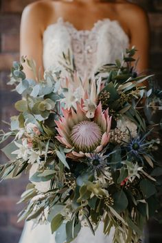 a bride holding a bouquet of flowers and greenery