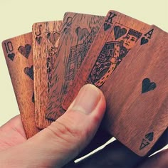 a hand holding four wooden playing cards in it's left hand, with the top one being held up