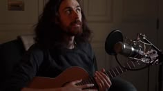 a man sitting in front of a microphone holding a guitar