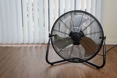 a black fan sitting on top of a hard wood floor next to a white window