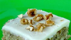 a piece of cake with white frosting and walnuts on top sitting on a green plate