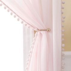 a pink sheer curtain with pom - poms hanging from it's side