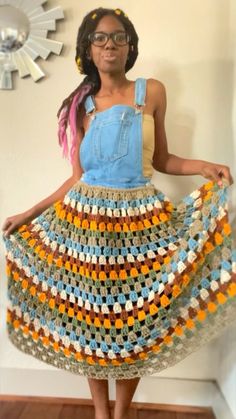 a woman is standing in front of a wall wearing a crocheted skirt and denim shirt