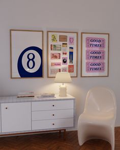 a white chair sitting next to a table with a lamp and pictures on the wall