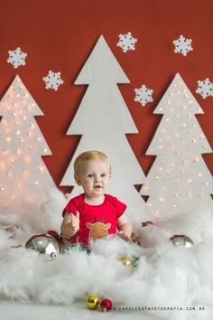 a baby sitting in front of christmas trees