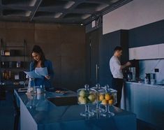 two people standing in a kitchen preparing food and looking at papers on the counter top