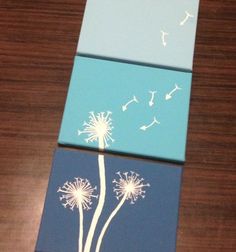 three paintings with dandelions on them sitting on top of a wooden table next to each other