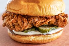 a fried chicken sandwich with pickles and mayonnaise on a bagel bun