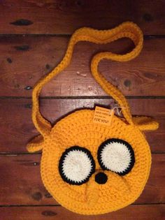 a yellow crocheted bag with eyes and a cord around the neck on a wooden floor