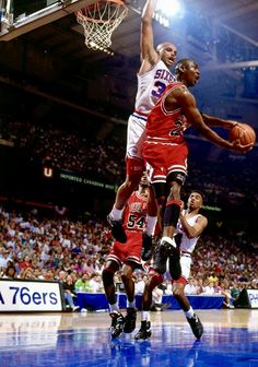 two men playing basketball in front of an audience at a sporting event, one is jumping up to dunk the ball