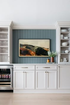 a kitchen with white cabinets and an art piece on the wall above the refrigerator door