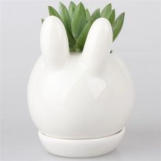 a white ceramic bunny shaped planter with green leaves