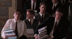 a group of young men standing next to each other in front of a wall holding books