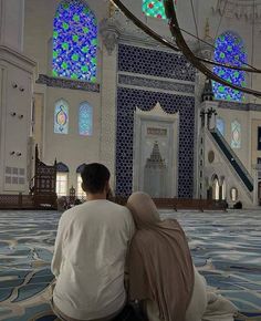 two people sitting on the ground in front of a building with blue and white stained glass windows