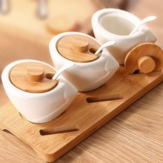 three white ceramic teapots with wooden spoons on a bamboo tray next to each other