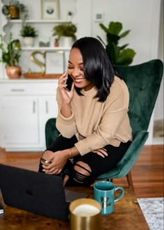 a woman sitting on a green chair talking on her cell phone and holding a laptop