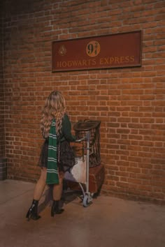 a woman standing in front of a brick wall next to a small cart with a dog on it