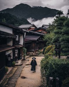 a woman with an umbrella walks down a path in front of some buildings on a cloudy day