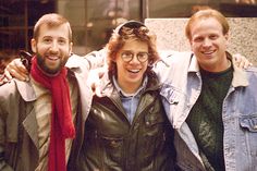 three men standing next to each other in front of a building