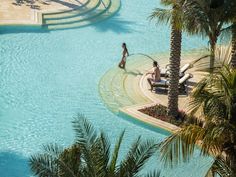 two people are sitting on lounge chairs in the pool next to palm trees and water