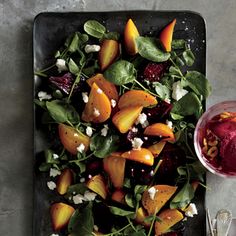 a salad with beets, spinach and goat cheese on a black plate next to a glass of red wine