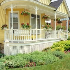 a yellow house with white railing and flowers on the front porch, next to green grass