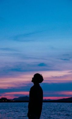 a person standing in front of a body of water at night with the sun setting