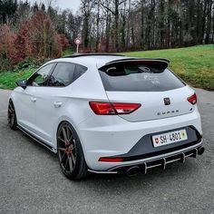 the rear end of a white car parked in a parking lot next to some trees