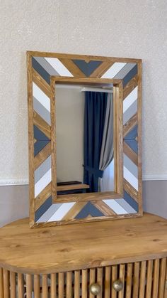 a mirror sitting on top of a wooden table next to a window with blue curtains