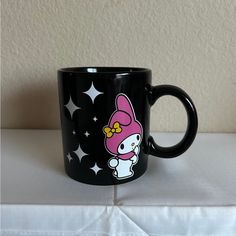 a hello kitty coffee mug sitting on top of a white table cloth with stars around it