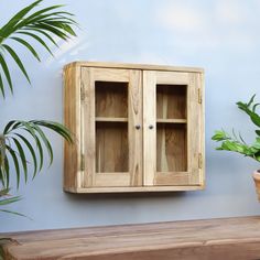 a wooden cabinet sitting on top of a wooden bench next to a potted plant