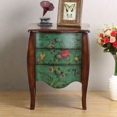 a green painted dresser with flowers on it next to a vase and flower arrangement in the corner