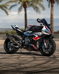 a red, white and blue motorcycle parked on the side of a road next to palm trees