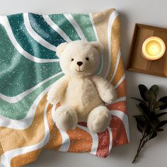 a white teddy bear sitting on top of a blanket next to a candle and plant