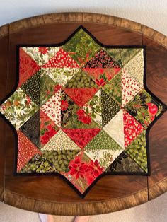 a wooden table topped with a patchwork quilt on it's side and a person standing next to it