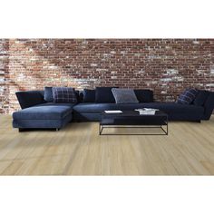 a living room with brick wall and wooden flooring, blue sectional sofa on the right side