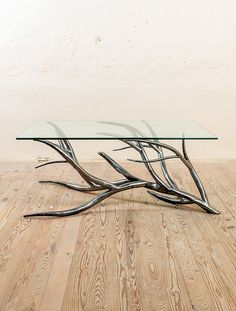 a glass table with metal branches on the top sitting on a wooden floor in front of a white wall