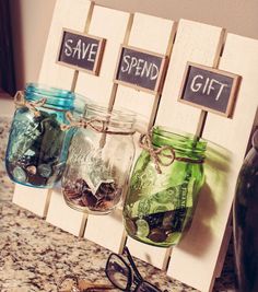 three mason jars filled with money sitting on top of a counter next to a pair of glasses