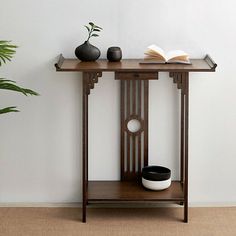 a table with an open book and vase on it next to a potted plant