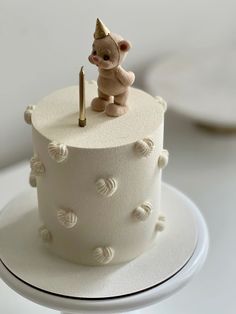 a small teddy bear sitting on top of a white cake