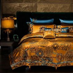 a bed with gold and blue comforters in a room next to a lamp on a table