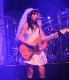 a woman in white dress playing guitar on stage