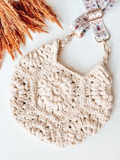 a crocheted purse sitting next to a dried plant on a white table top