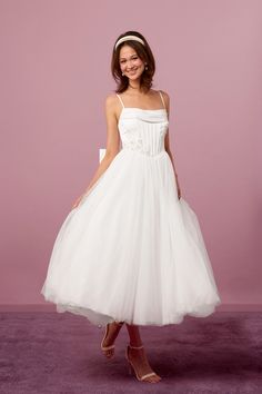 a woman wearing a white dress and headband posing in front of a pink background