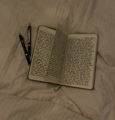 an open book with writing on it and a pen laying next to it sitting on a bed