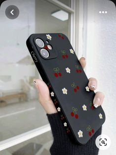 a woman holding up her phone case with cherries and daisies on the back