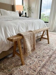 a wooden bench sitting on top of a bed next to a large window in a bedroom