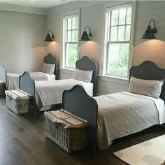 two twin beds in a room with wooden floors and white walls, along with three windows